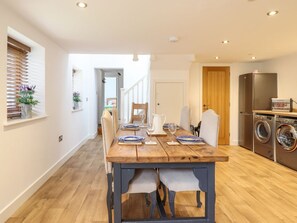 A modern kitchen with a wooden table, built-in washing machine, and a view to the dining area. - The Granary, Llandyssil, Powys (Montgomery)