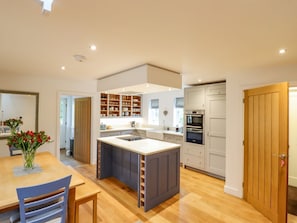 A modern kitchen with a central island, built-in appliances, and a dining area with a table and chairs. - Fern Cottage, Elsworth, Cambridge (Cambridge)