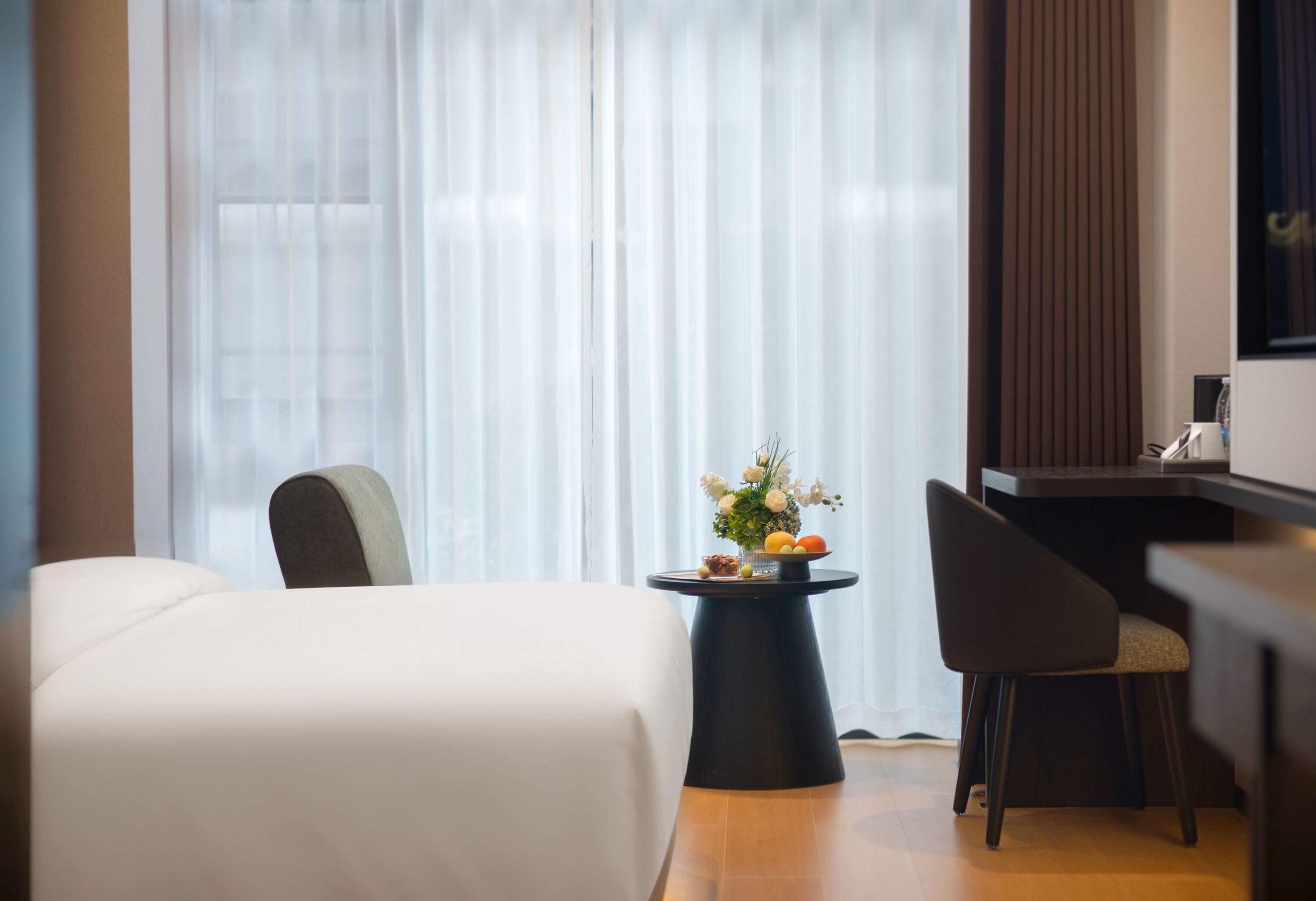 Habitación de hotel con cama, escritorio, silla y una mesita con un florero.