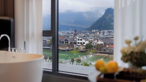 A bathroom with a large window offering a view of a town and mountains. - Forest Oxygen Bar Resort Hotel (Zhangjiajie)