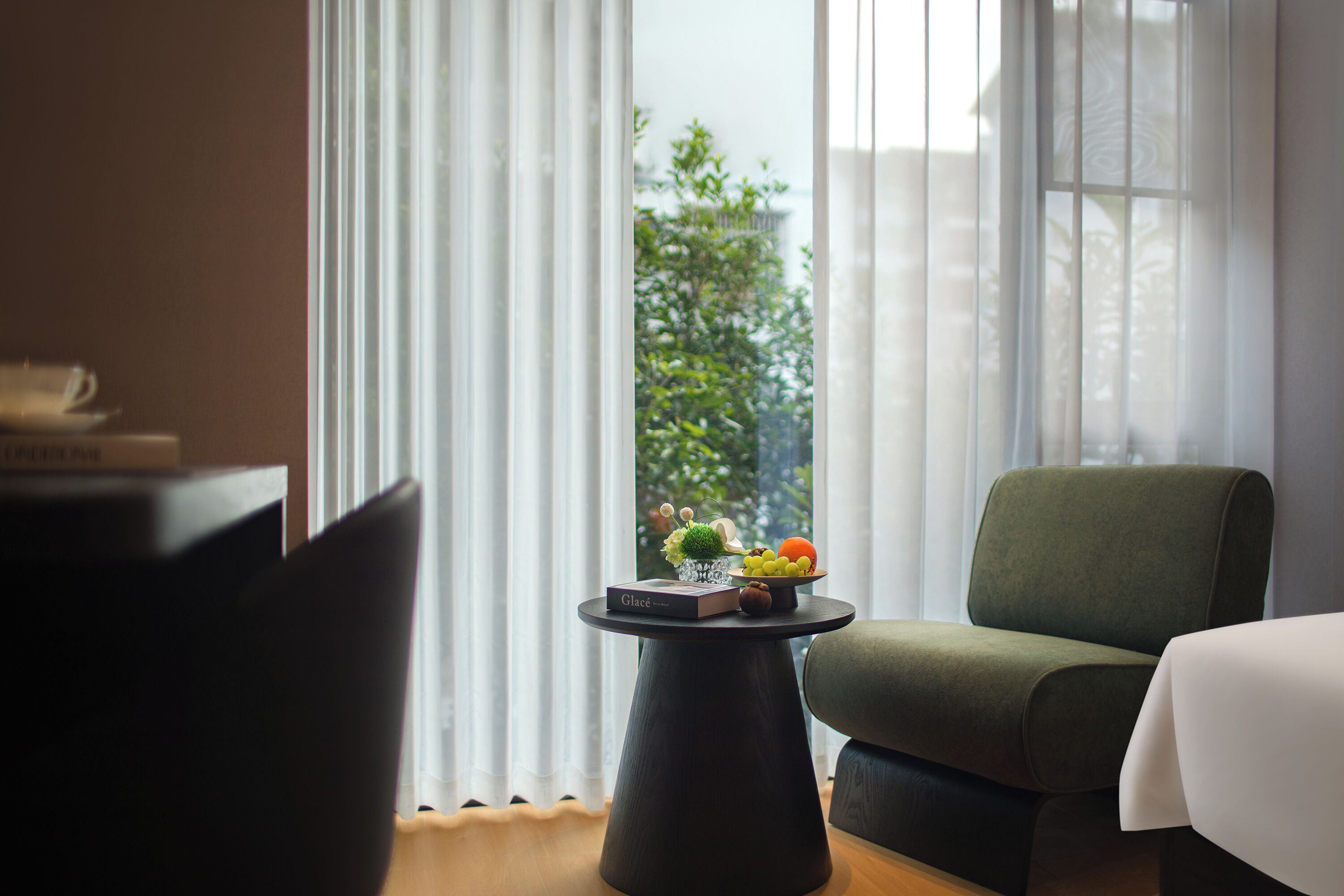 Een moderne kamer met een ronde tafel, een groene fauteuil en uitzicht door grote ramen.