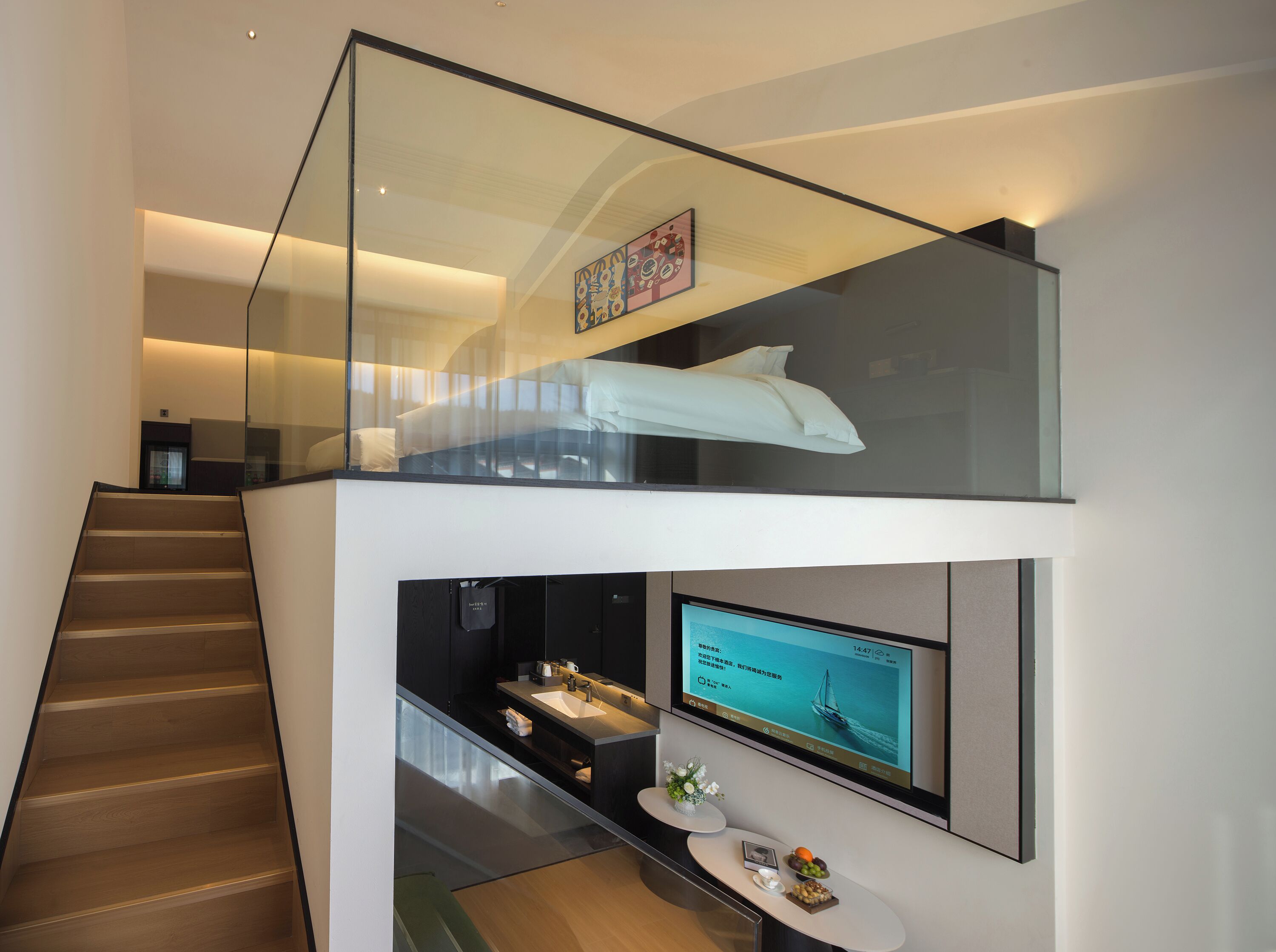 Un intérieur moderne avec un escalier, une balustrade en verre, un téléviseur à écran plat et un lit avec un oreiller blanc.
