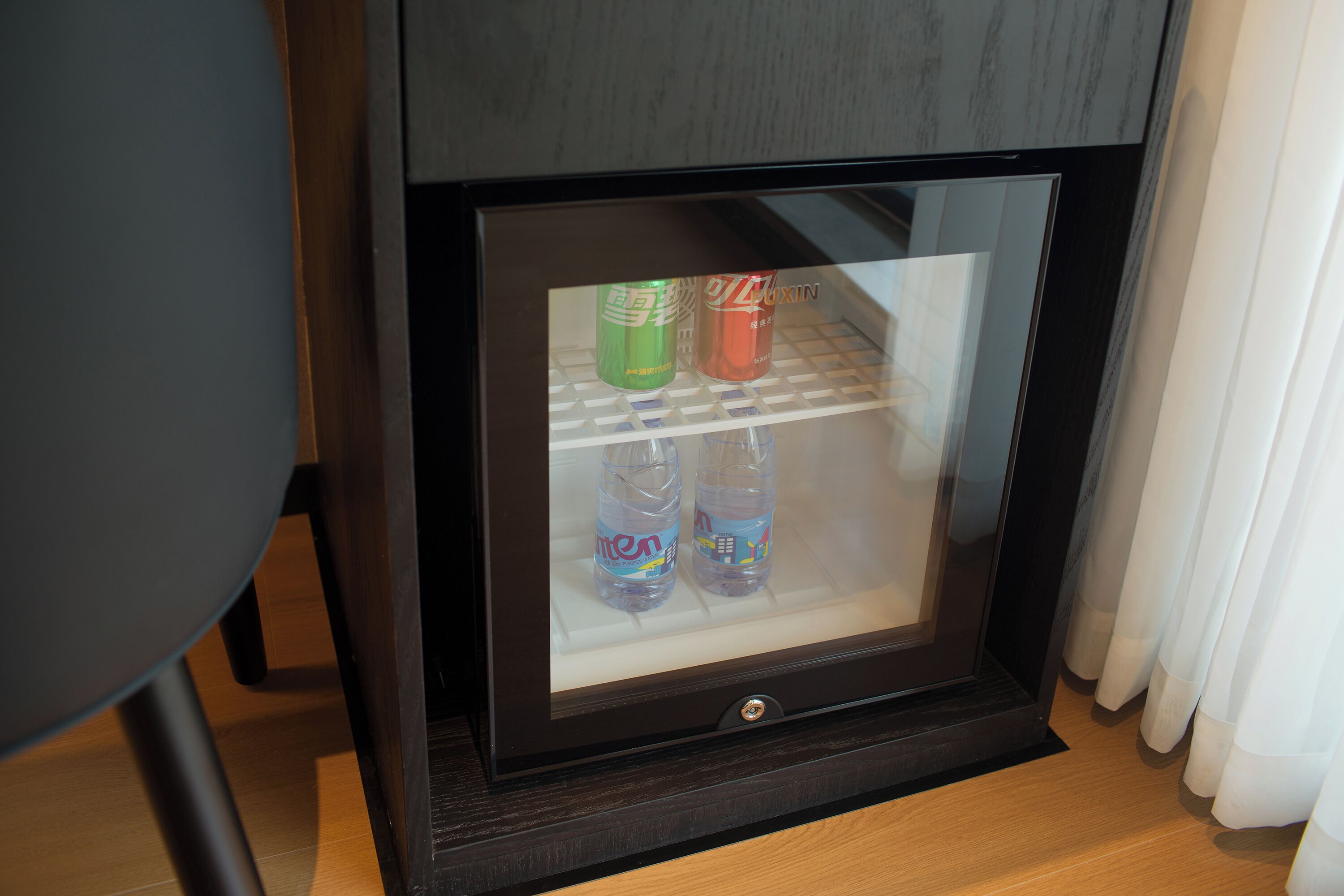 Een minibar met glazen deur, met daarin twee waterflesjes en een fles frisdrank.