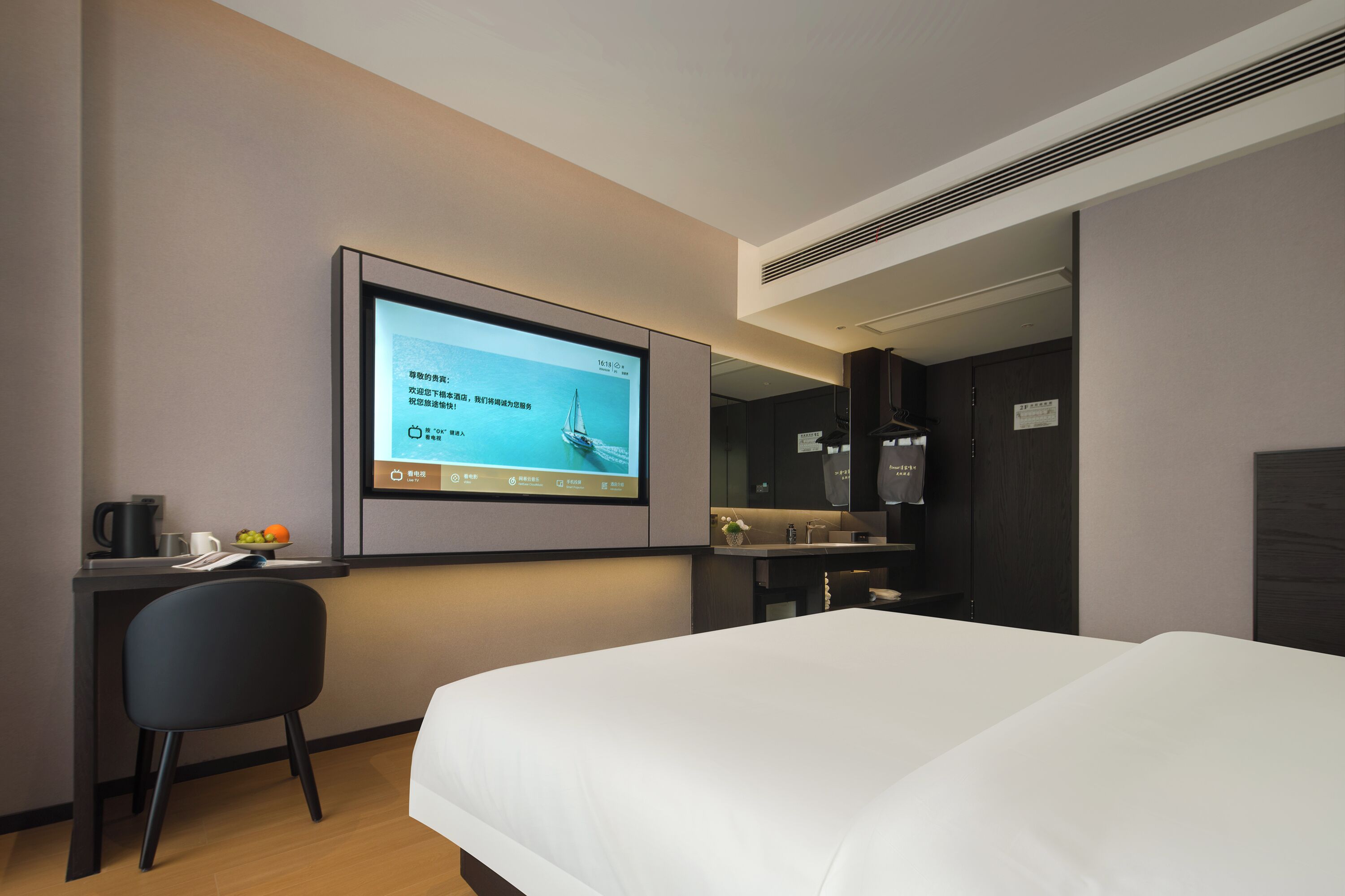 Habitación de hotel con cama, escritorio con monitor de computadora, una silla y una pequeña zona de kitchenette.