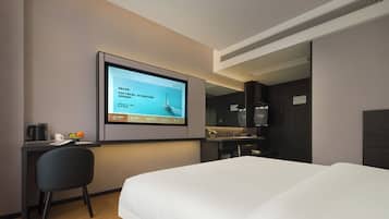 Habitación de hotel con cama, escritorio con monitor de computadora, una silla y una pequeña zona de kitchenette.
