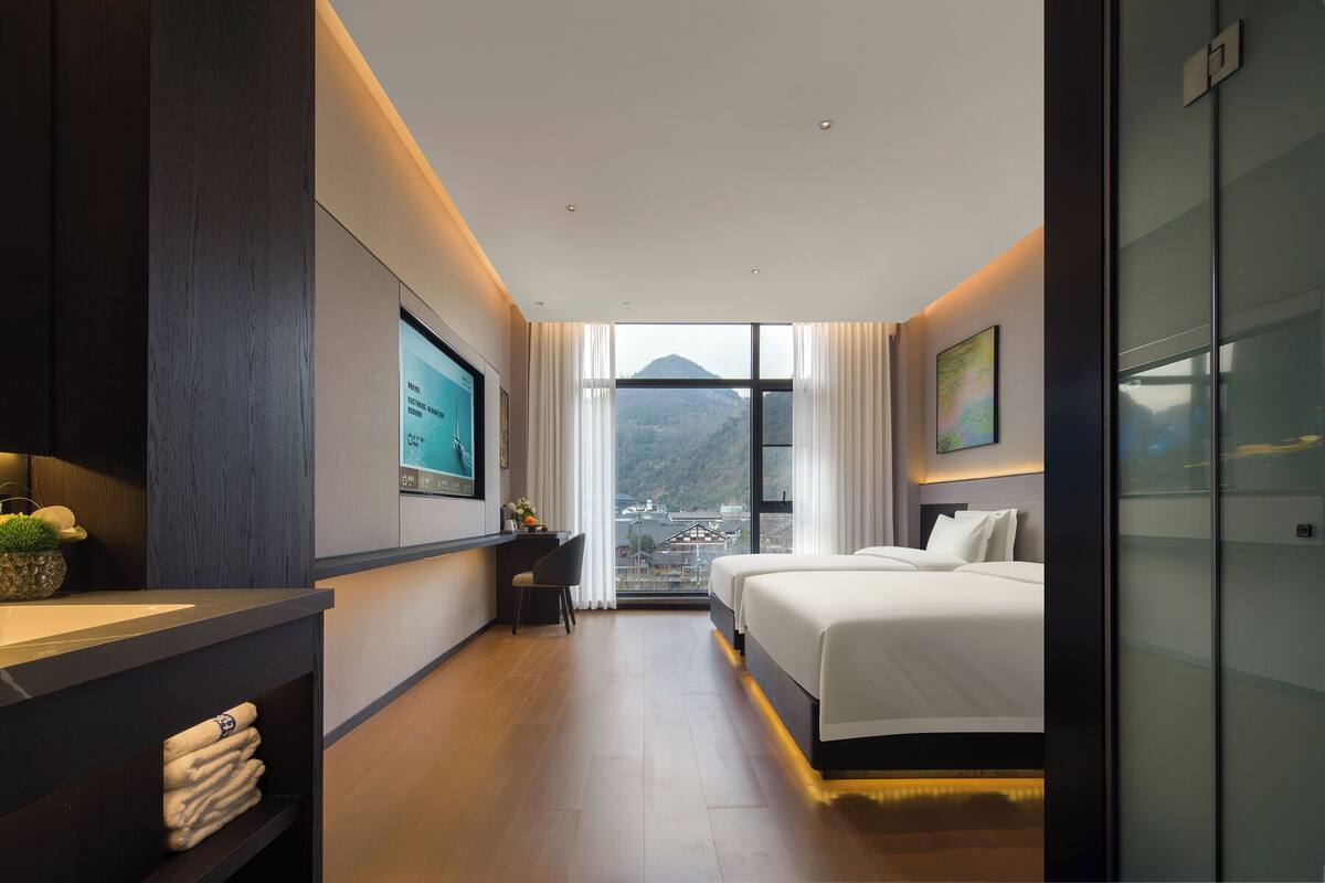 Quarto de hotel moderno com uma cama grande, uma escrivaninha, uma cadeira e vista para uma montanha.