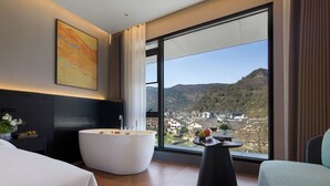 A modern hotel room with a large window, a bathtub, a dining table, and a chair. - Forest Oxygen Bar Resort Hotel (Zhangjiajie)