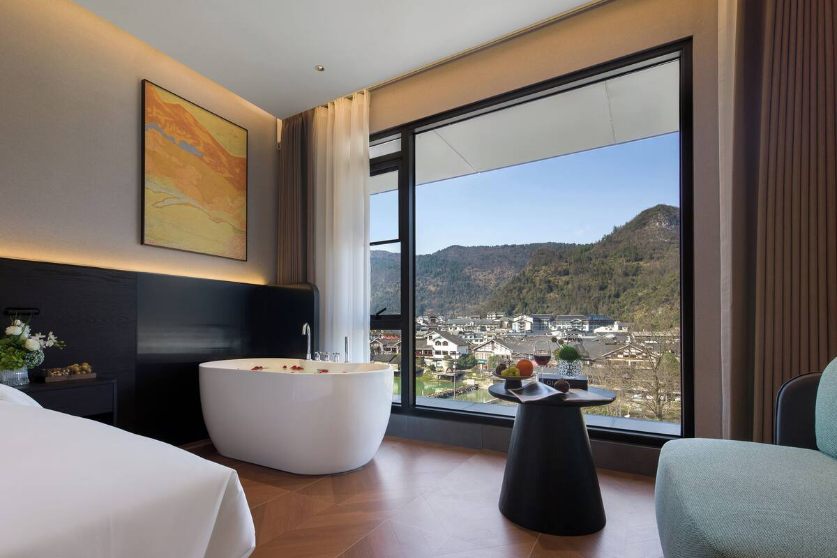 Quarto de hotel moderno com uma janela grande, uma banheira, uma mesa de jantar e uma cadeira.