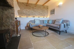 Ein gemütliches Wohnzimmer mit einer Steinwand, einer Couch mit vielen Kissen, einem runden Couchtisch und einem Kamin.