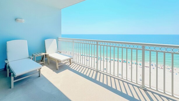 A balcony with two white lounge chairs, a white railing, and a view of a beach with people and umbrellas. - Colonnades 1403 | Completely updated! Gorgeous condo, beachfront, sleeps 12! (Gulf Shores)