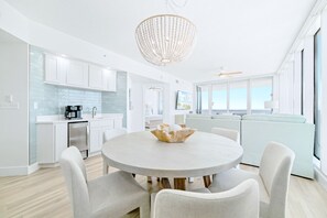 Une cuisine moderne avec des meubles blancs, un coin repas doté d’une table ronde et une vue sur la mer grâce à de grandes fenêtres.