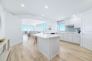 Une cuisine moderne avec des meubles blancs, un grand îlot central et un coin repas offrant une vue agréable.