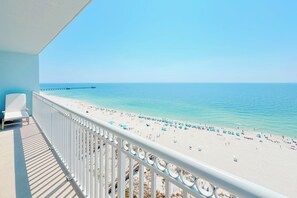 Un balcon avec vue sur une plage, une jetée au loin et un ciel dégagé.