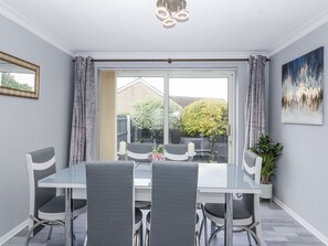 A dining area with a table and chairs, a window with curtains, a potted plant, and a painting on the wall. - Charming Zadena in Timsbury (Bath)