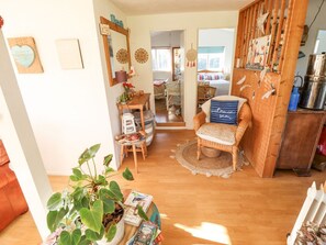 A cozy living room with a wicker chair, a table with books and a plant, and a wooden cabinet.