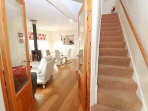A staircase leading to a second floor, a living room with a sofa and chairs, a fireplace, and a dining area.