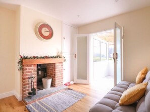 A living room with a fireplace, a sofa, and a door leading to an outdoor area. - Charming Woodview Home Near Grove Fm (Norwich)