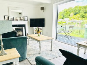 Un salon avec une cheminée, un téléviseur, une table ornée d’un vase et une vue sur un lac.