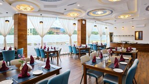 A restaurant with tables set for dining, large windows with curtains, and a view of a body of water. - Hotel HTC Thimphu (Thimphu)