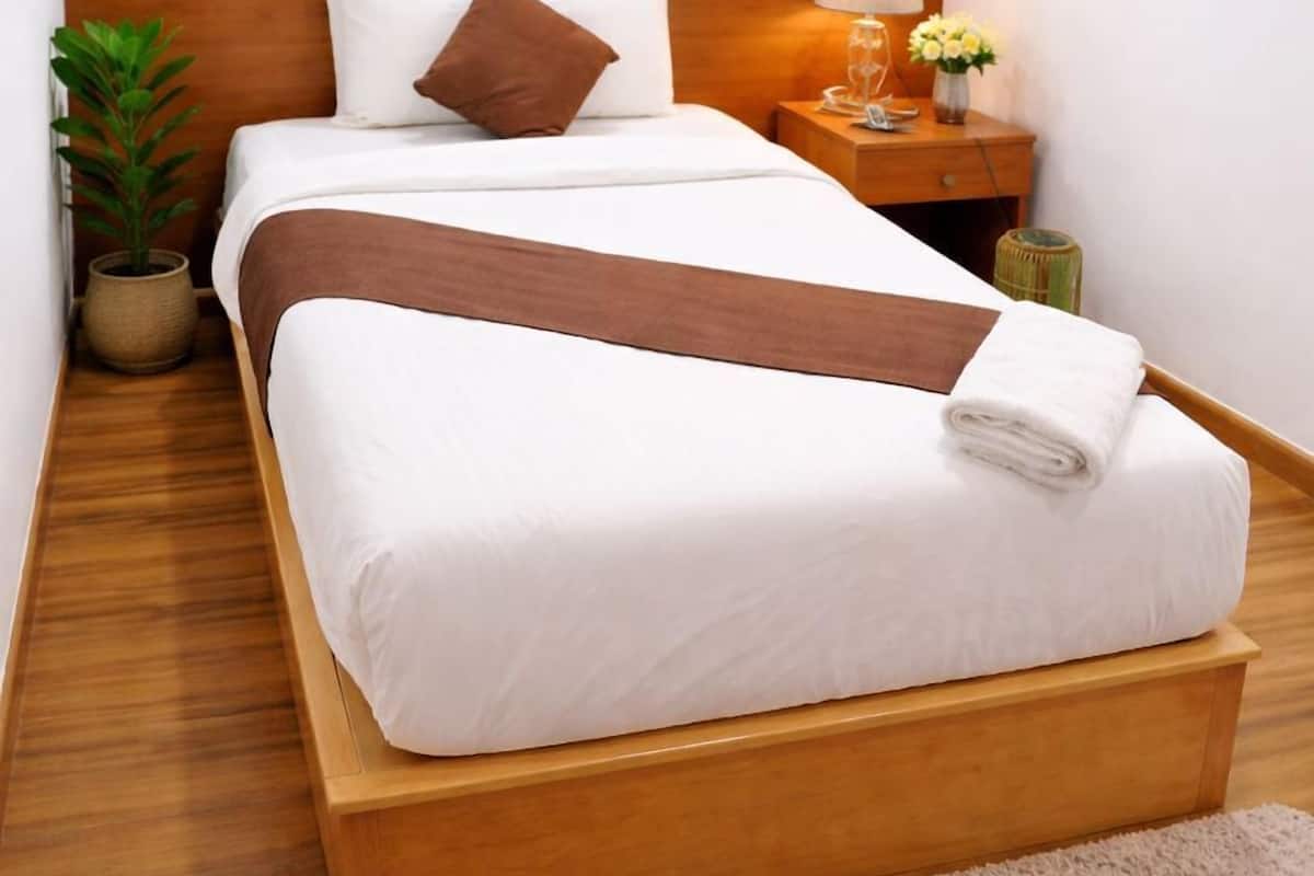A neatly made bed with a wooden headboard, a bedside lamp, a small table with a vase of flowers, and a painting on the wall.
