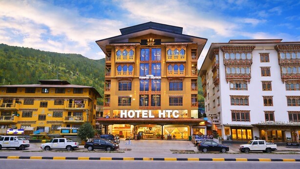A multi-story hotel with a prominent 'HOTEL HTC' sign, a parking lot, and a mountainous backdrop. - Hotel HTC Thimphu (Thimphu)