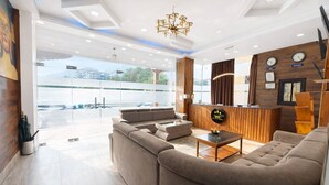 A modern hotel lobby with a reception desk, seating area, and large windows offering a view of the parking lot. - Hotel HTC Thimphu (Thimphu)