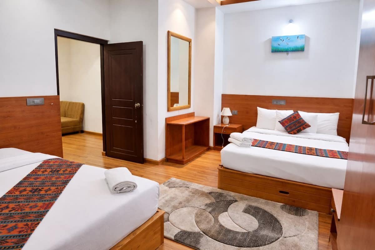 A hotel room with two beds, a wooden headboard, a nightstand, a mirror, and a painting on the wall.