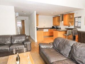 A modern living room with two leather sofas, a coffee table with a bottle and glasses, and a kitchen area with wooden cabinets and a microwave. - Durham Cottage, in Wolsingham. (Bishop Auckland)