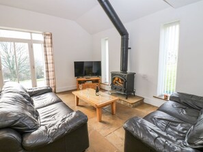 A living room with leather sofas, a wooden coffee table, a TV, and a black wood-burning stove. - Durham Cottage, in Wolsingham. (Bishop Auckland)