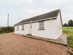 A white single-story house with a tiled roof, a gravel driveway, and a small front porch.