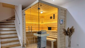 Ein modernes Interieur mit einer Holztreppe, einem durch Glas abgetrennten Raum mit einer Bank, einem kleinen Tisch und einer Topfpflanze.