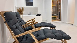 Ein modernes Wohnzimmer mit einer Couch, einem Stuhl mit Holzrahmen, einer weißen Wand und einem Badezimmer mit Badewanne und Holzvertäfelung.