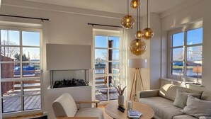 Ein modernes Wohnzimmer mit Sofa, Sessel, Couchtisch, Kamin und großen Fenstern.