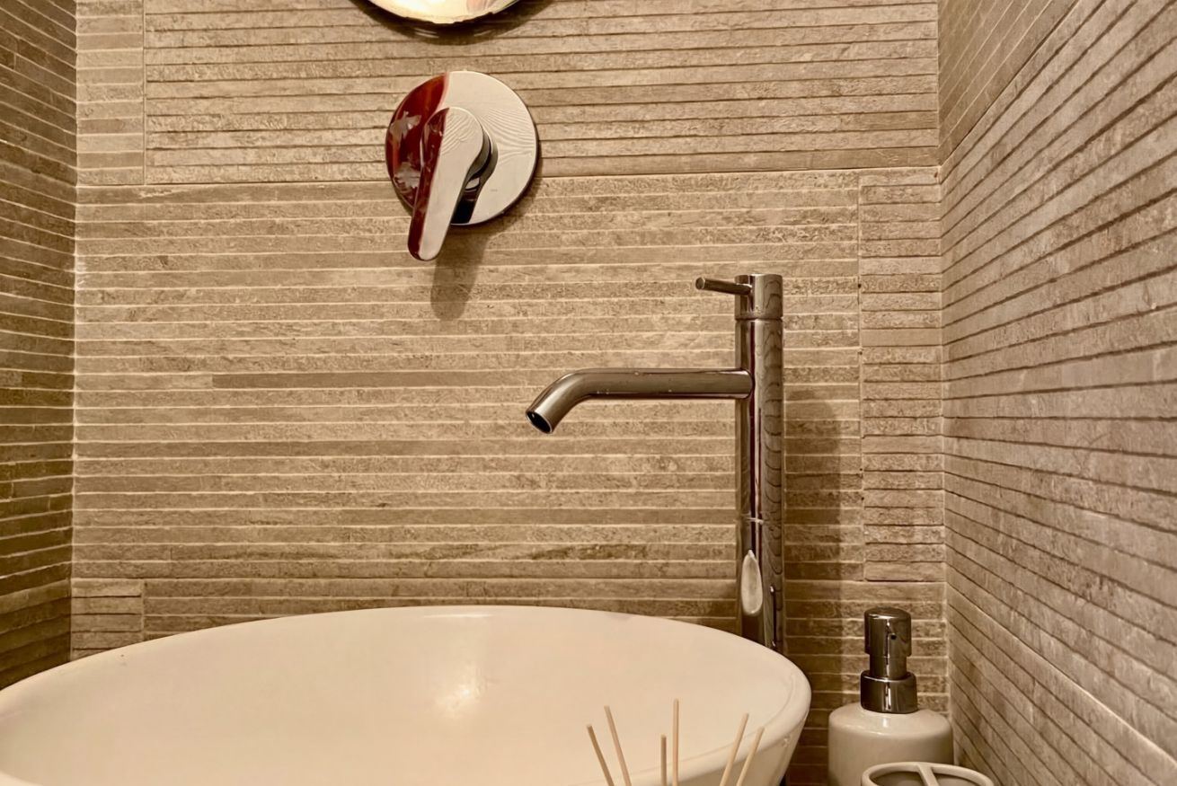 Un baño con un lavamanos blanco, un grifo moderno y un dispensador de jabón en la pared.