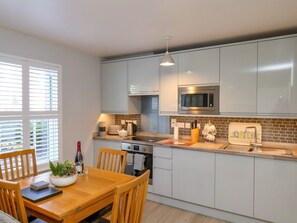 A modern kitchen with white cabinets, a built-in microwave, and a dining area with a wooden table and chairs. - Denby Seahaven, Primrose Valley (Filey)