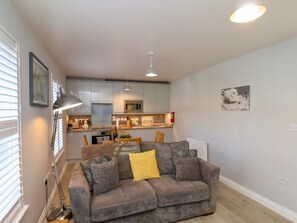 A living room with a grey sofa, a floor lamp, and a kitchen in the background. - Denby Seahaven, Primrose Valley (Filey)