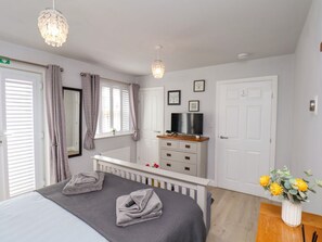 A bedroom with a bed, a TV, a dresser, a radiator, and a window with curtains. - Denby Seahaven, Primrose Valley (Filey)