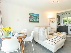 A modern living room with a sofa, dining table, and chairs, a painting on the wall, and a kitchen in the background. - Gull Cottage, Kessingland (Lowestoft)