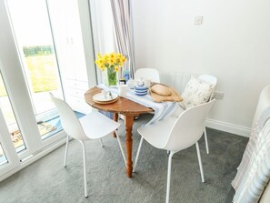 A dining area with a table, chairs, a vase of flowers, and a view through a glass door. - Gull Cottage, Kessingland (Lowestoft)