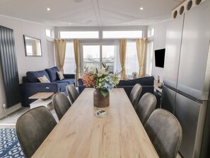 A modern hotel room with a dining table, sofa, and a large window with curtains. - Caravan 195D, Newcastle, County Down (Newcastle)