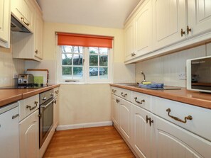 A kitchen with white cabinets, a window with an orange blind, a toaster, and a microwave.
