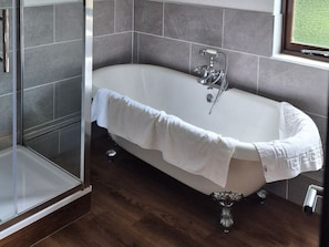 Une salle de bain moderne avec une baignoire sur pieds, une douche à parois de verre et une fenêtre laissant entrer la lumière naturelle.