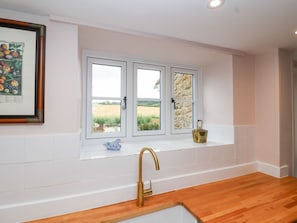 Eine Küche mit weiß gefliestem Spritzschutz, einer Holzarbeitsplatte, einem goldenen Wasserhahn und einem Fenster mit Blick auf ein Feld.