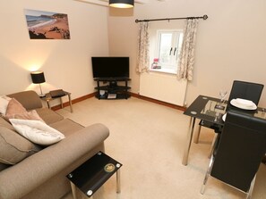 Ein Wohnzimmer mit einer Couch, einem Fernseher, einem Tisch mit einem Glas und einem Fenster mit Vorhängen.