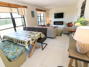 Ein Wohnzimmer mit einer Couch, einem Tisch und einem Fernseher. Ein Fenster bietet einen Ausblick nach draußen.