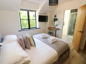 Ein Schlafzimmer mit Bett, Kissen, Fernseher, Spiegel, Holztür und Fenster.