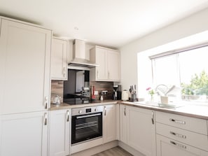 A modern kitchen with white cabinetry, a built-in oven, and a window providing natural light. - Clyne Cottage, Elgin (Elgin)