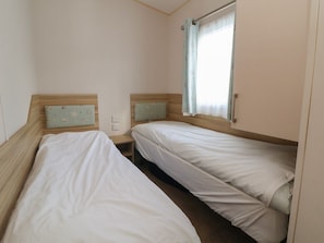 A small, single-room accommodation with two single beds, a window with curtains, and a wooden headboard.