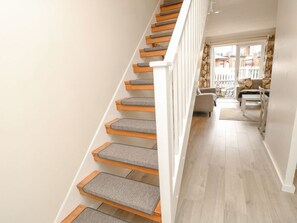 Una escalera con escalones de madera y barandillas cubiertas de moqueta gris, que conduce a una sala de estar con sofá y una mesa de centro.