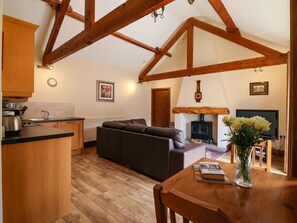 A kitchen with wooden beams, a sofa, a dining table with a book and flowers, a fireplace, and a television. - Winsall Court II: Cozy Ground Floor Retreat (Driffield)